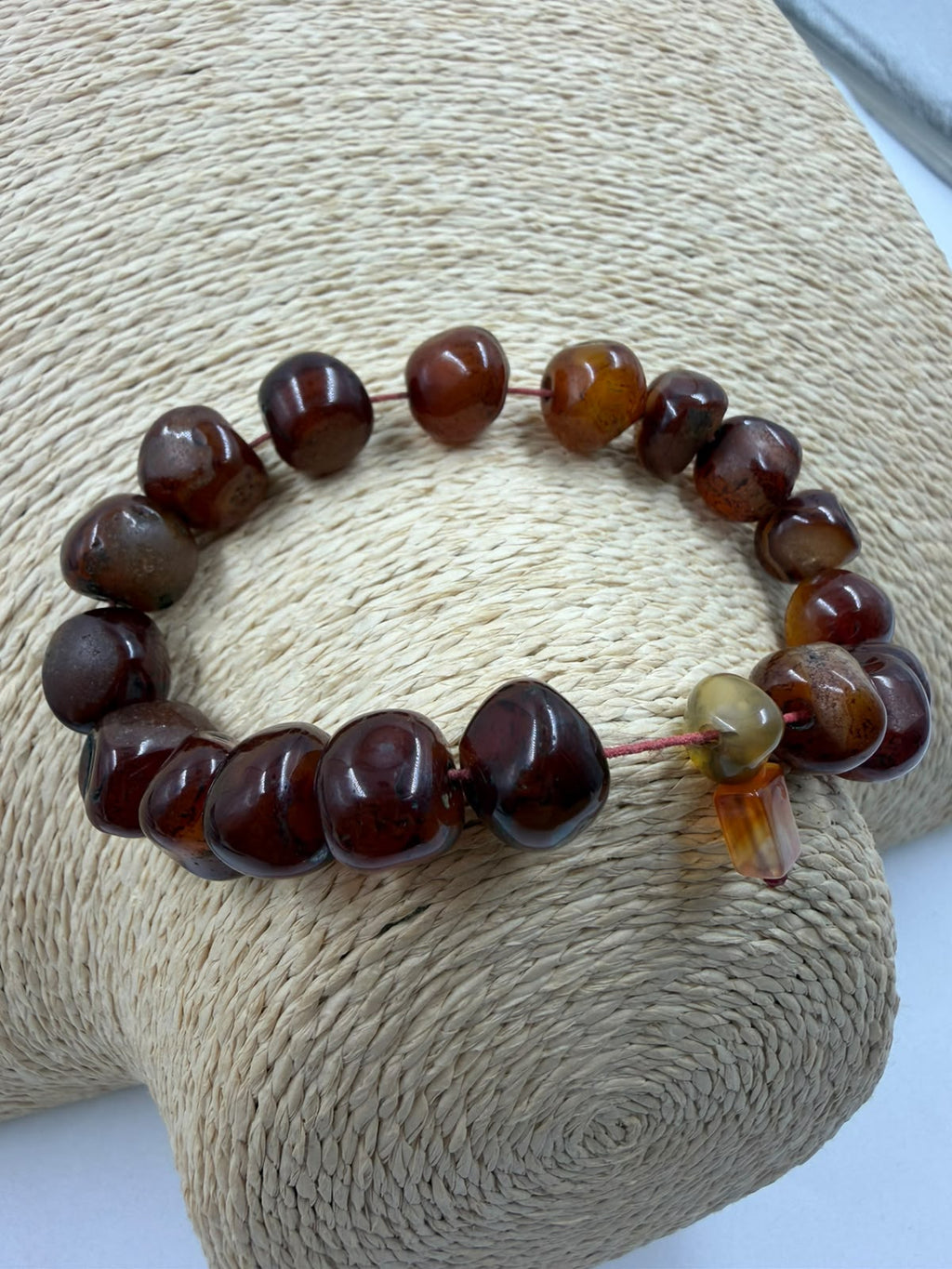 Natural red agate tumbled bracelet side view in hand showing all beads stopper and red cord detail