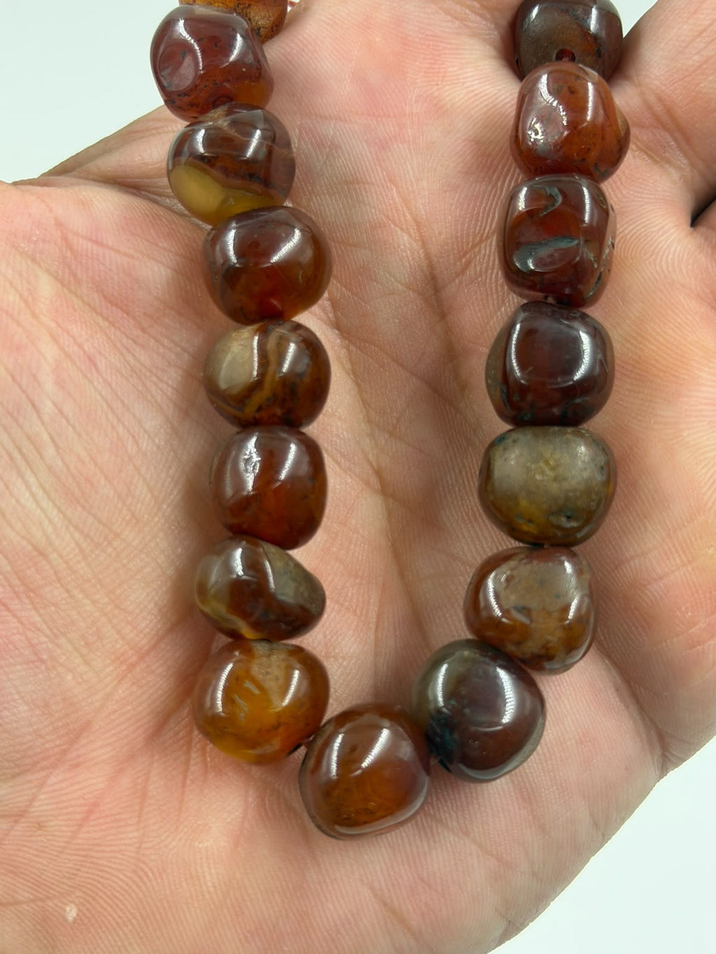 Natural red agate tumbled bracelet on rattan showing deep burgundy color and organic bead shapes