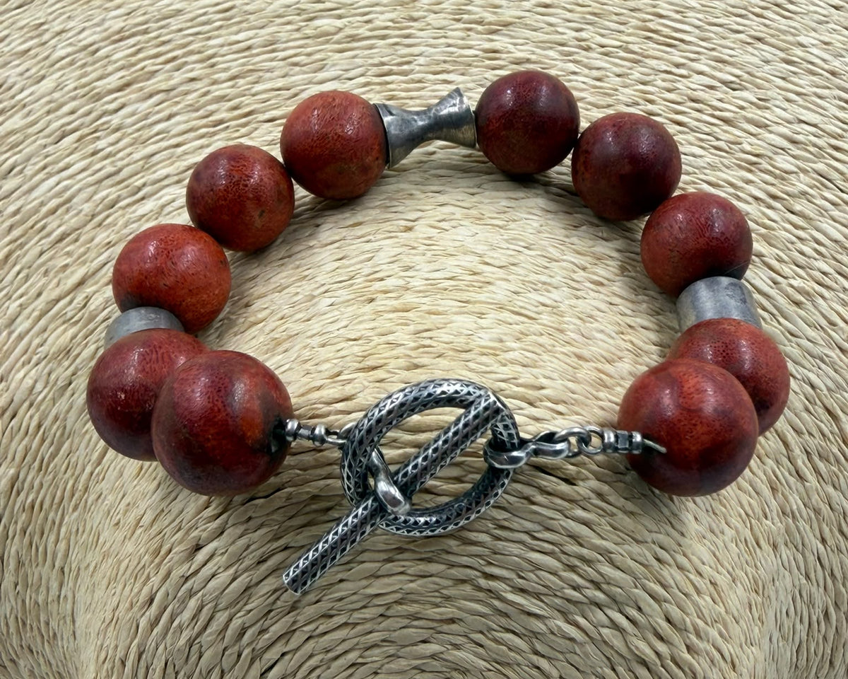 Natural red coral bracelet held in hand side view showing full length 23.5cm open and bead size scale