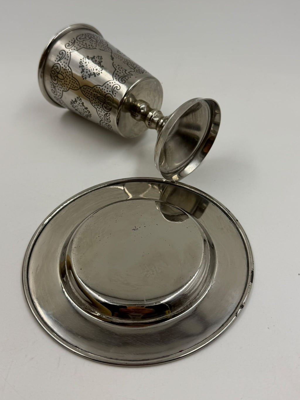 Israeli silver-plated Kiddush cup held in hand showing arabesque engravings close-up