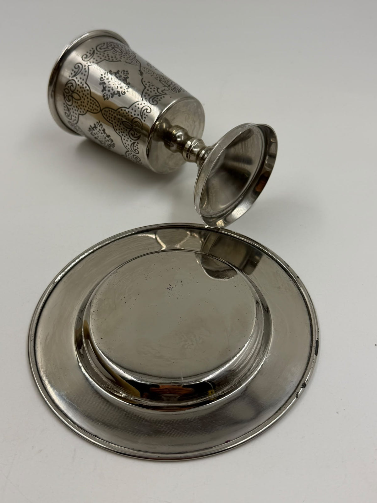 Israeli silver-plated Kiddush cup held in hand showing arabesque engravings close-up