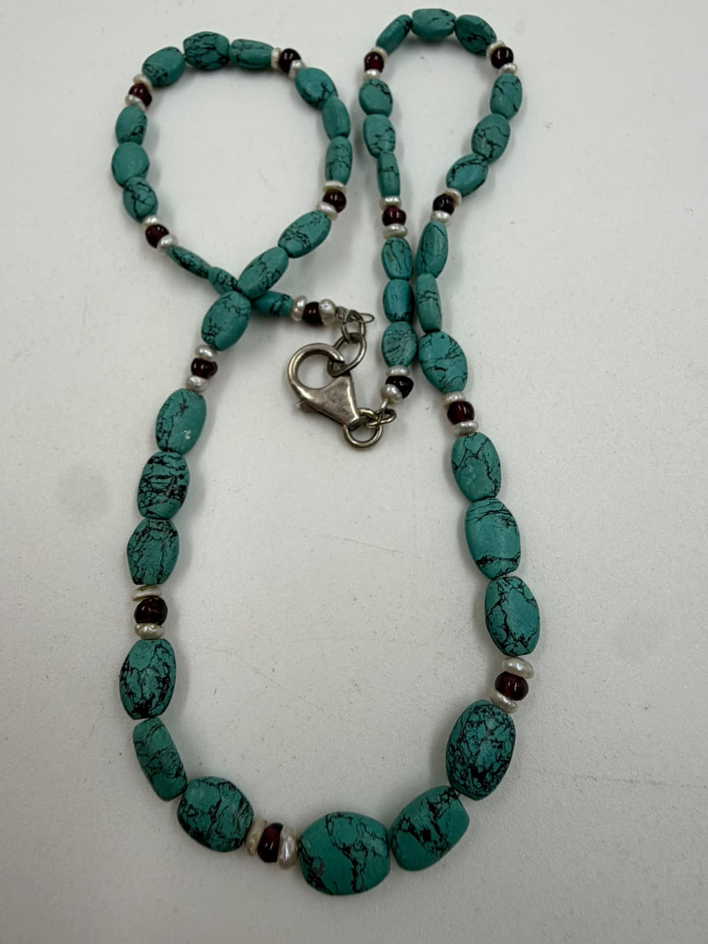 Close-up of natural turquoise oval nuggets with black matrix veining garnet and pearl spacers