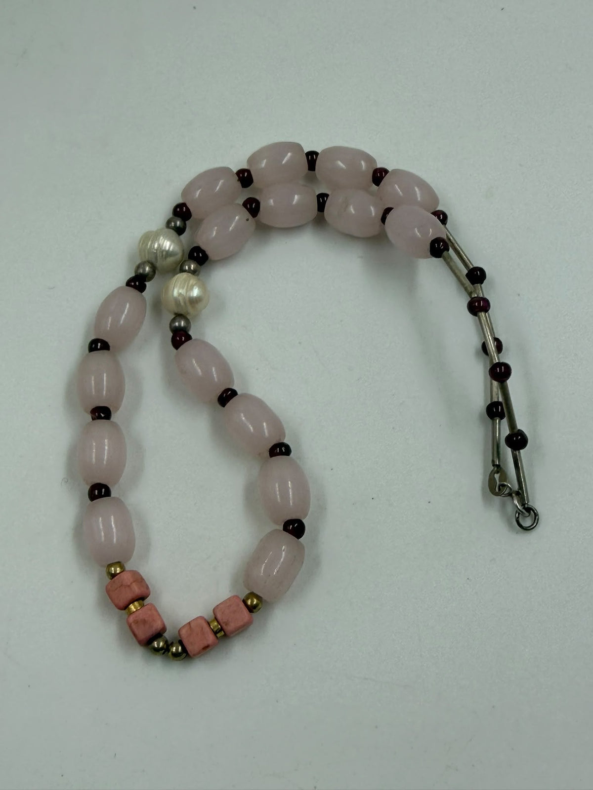 Natural rose quartz oval barrel bracelet coiled on white background showing garnet beads and coral cubes