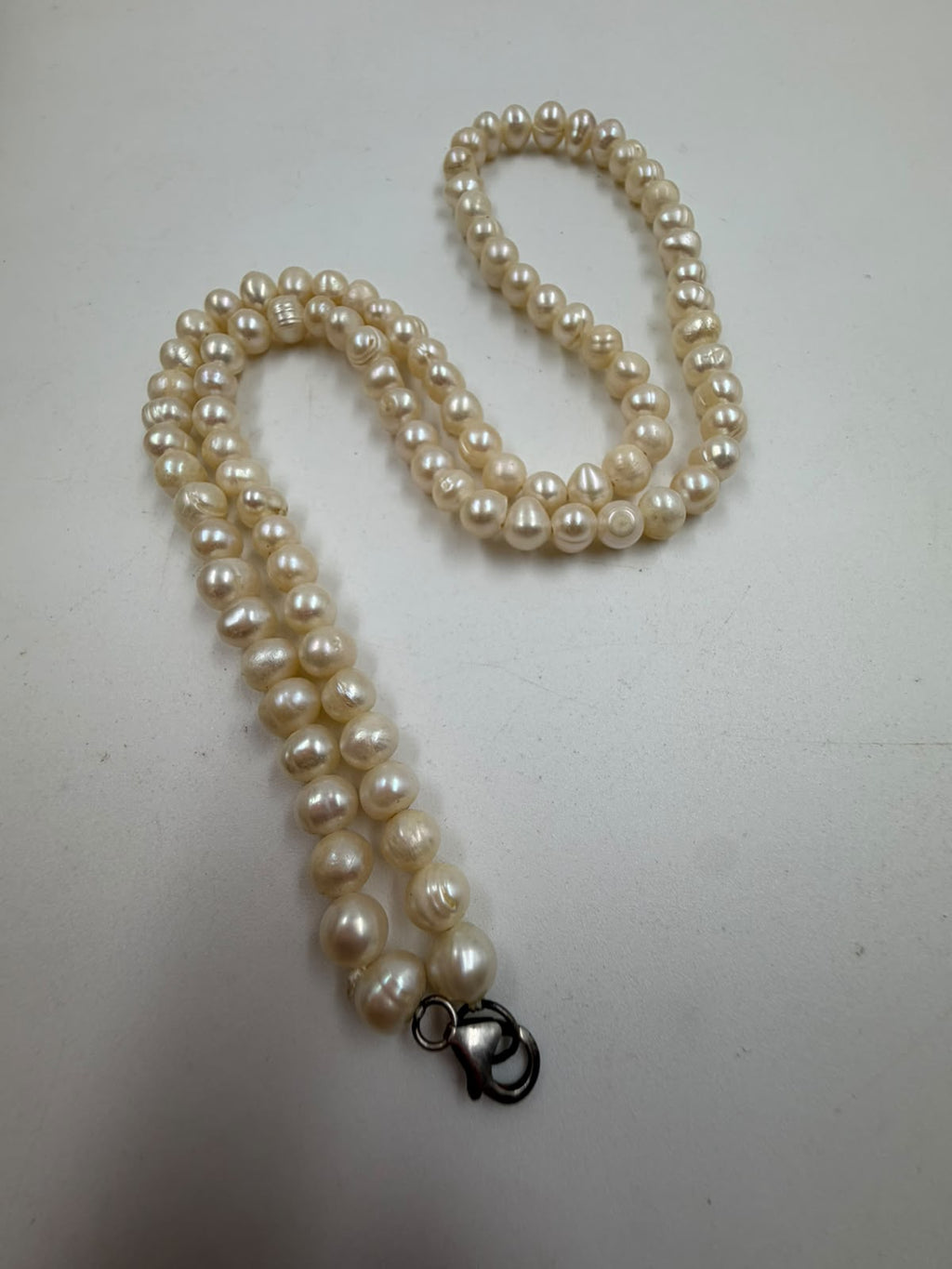 Freshwater pearl necklace coiled on white surface showing all beads and lobster clasp ring