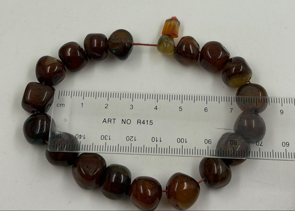 Natural red-brown agate tumbled bracelet on rattan display showing freeform beads and red cord full view